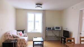 A living room with a sofa, a coffee table, a TV, a microwave, and a dining table with chairs.