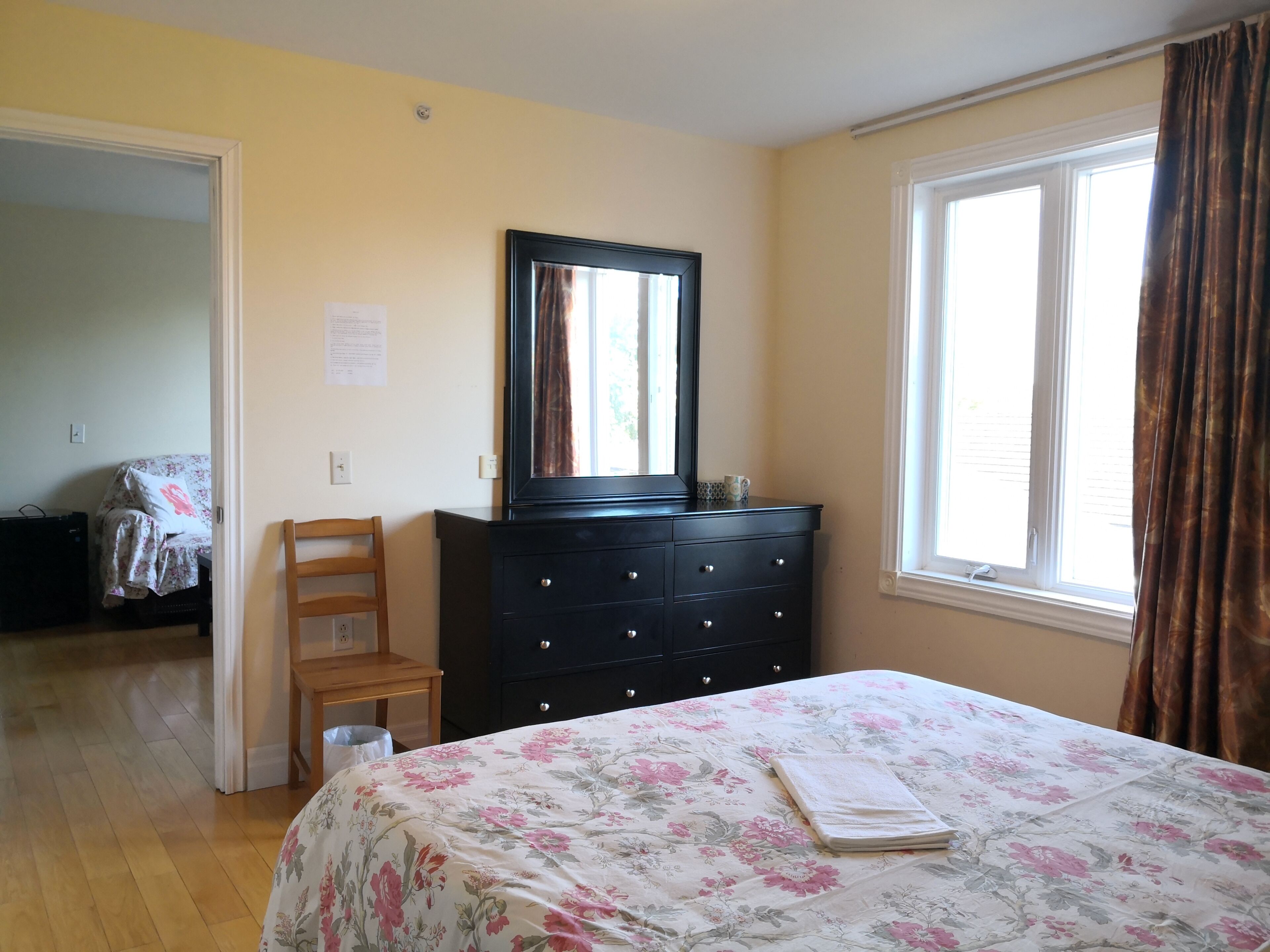 Une chambre à coucher avec un lit, une commode, une chaise, une fenêtre et une porte.