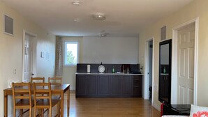 A spacious living area with a wooden dining table and chairs, a kitchen with dark cabinets, and a large window.