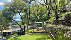 A deck with outdoor furniture overlooking a body of water, surrounded by lush greenery and trees. - Fika Cabin - Boscata (petfriendly) (El Oasis Valsequillo)