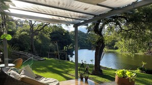 A covered outdoor seating area with wicker furniture and a view of a lake. - Fika Cabin - Boscata (petfriendly) (El Oasis Valsequillo)