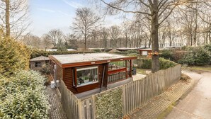 Eine moderne Holzhütte mit großem Fenster, umgeben von dichtem Grün und einem Holzzaun.