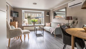 Ein modernes Wohnzimmer mit einer Couch, Sesseln, einem Esstisch und einem großen Fenster mit Blick ins Freie.