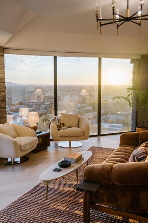 Ein geräumiges Wohnzimmer mit hoher Decke, großen Fenstern mit Blick auf die Stadt, einem modernen Kronleuchter und einer Mischung aus zeitgenössischen Möbeln.