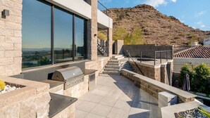 Eine moderne Terrassengrundstück mit Grill, großen Fenstern und Blick auf eine hügelige Landschaft.