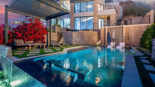 Ein modernes Haus mit Swimmingpool, Sitzgelegenheiten im Freien und Blick auf die umliegende Landschaft.