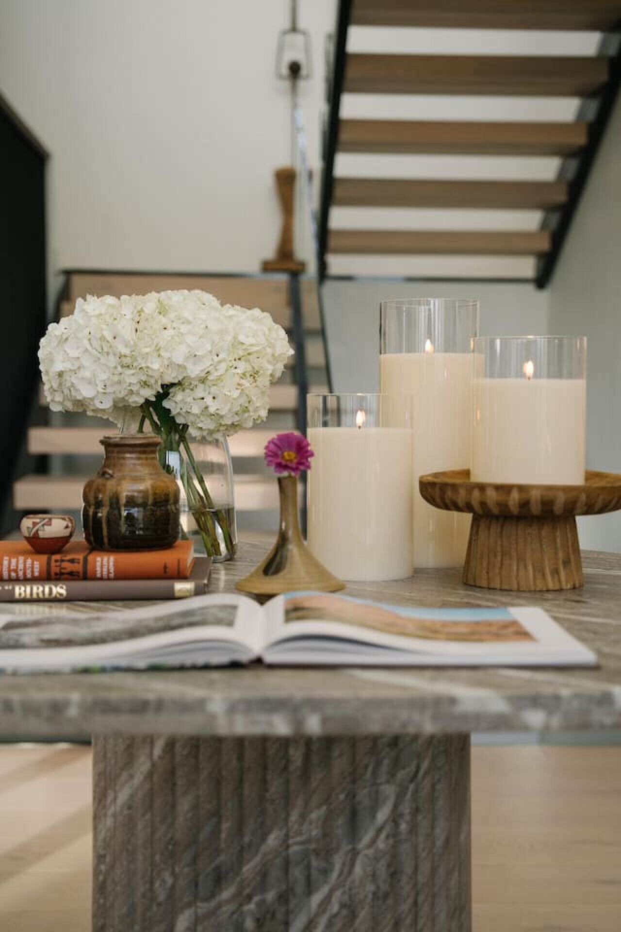 A marble-topped table with a book, a vase with white flowers, and two candles on a wooden stand.