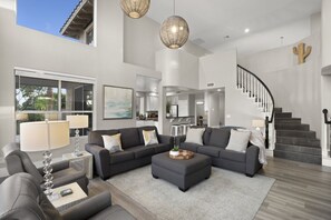 Ein geräumiges Wohnzimmer mit einer grauen Sofagarnitur, einem Couchtisch und einer Treppe, die zu einer oberen Ebene führt.