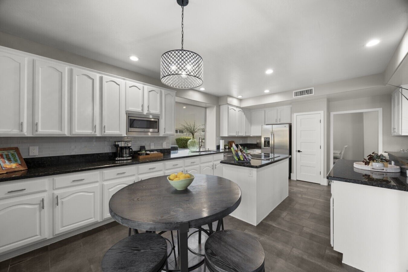 A modern kitchen with white cabinetry, a central island with stools, and a hanging light fixture.