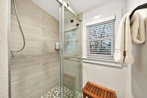 Eine gläserne Duschkabine mit Handbrause, einer Holzbank und einem Fenster mit Jalousien.