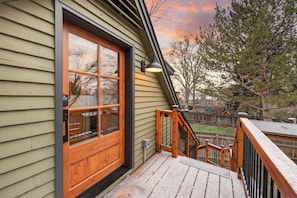 Une porte d’entrée en bois avec un panneau de verre, une terrasse en bois et une rambarde en métal.