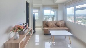 A spacious living room with a sofa, a coffee table, and a view of the city through large windows. - Mashley Room at Serpong Garden Apartment (Cisauk)
