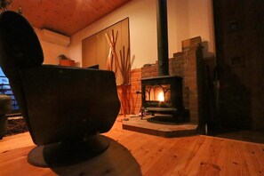 A cozy room with a wooden table, a black chair, a brick fireplace, and a wooden ceiling. - Izu-atami Ocean View House (Atami)