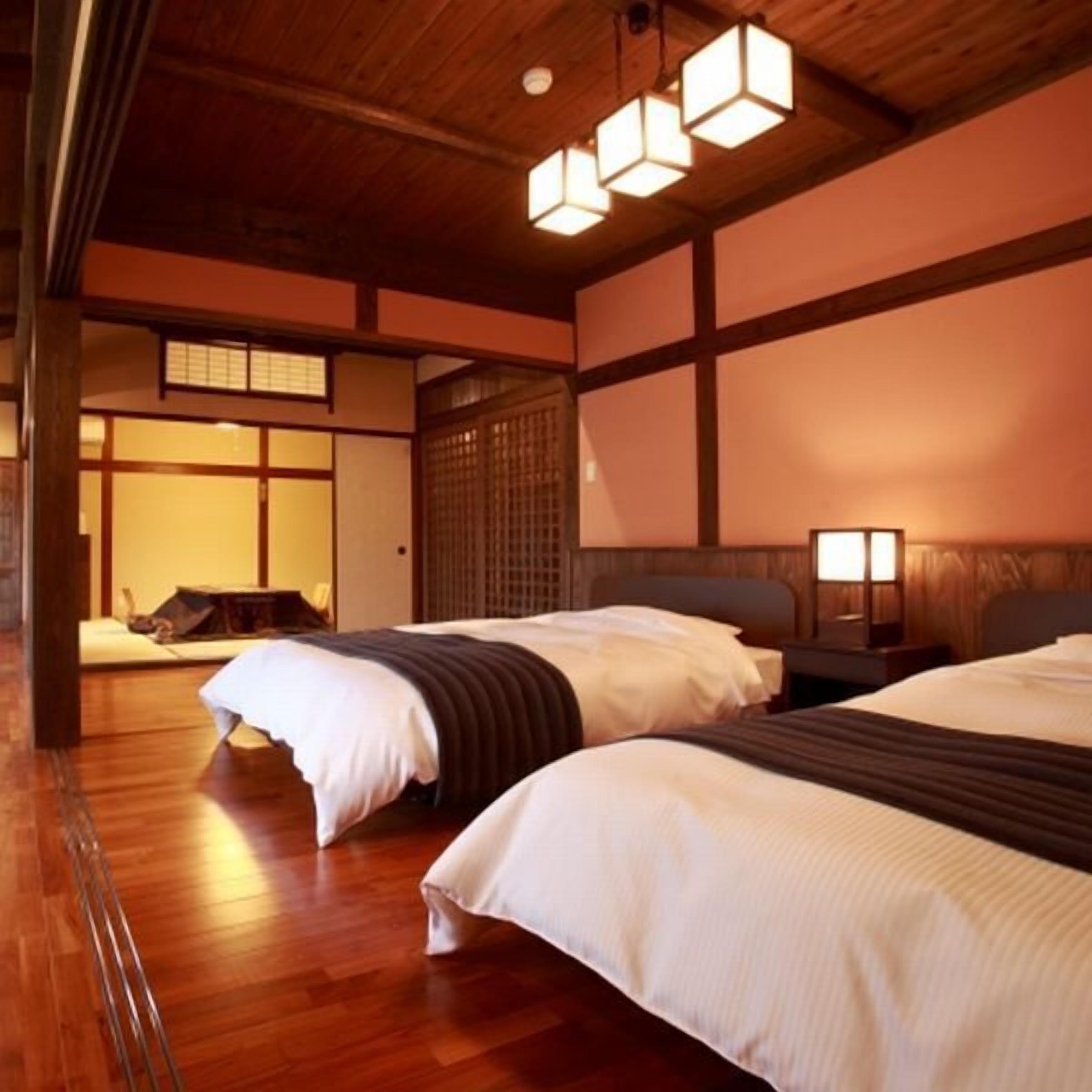 A traditional Japanese-style room with wooden floors, tatami mats, and a low ceiling. There are two beds with white bedding and a wooden headboard.