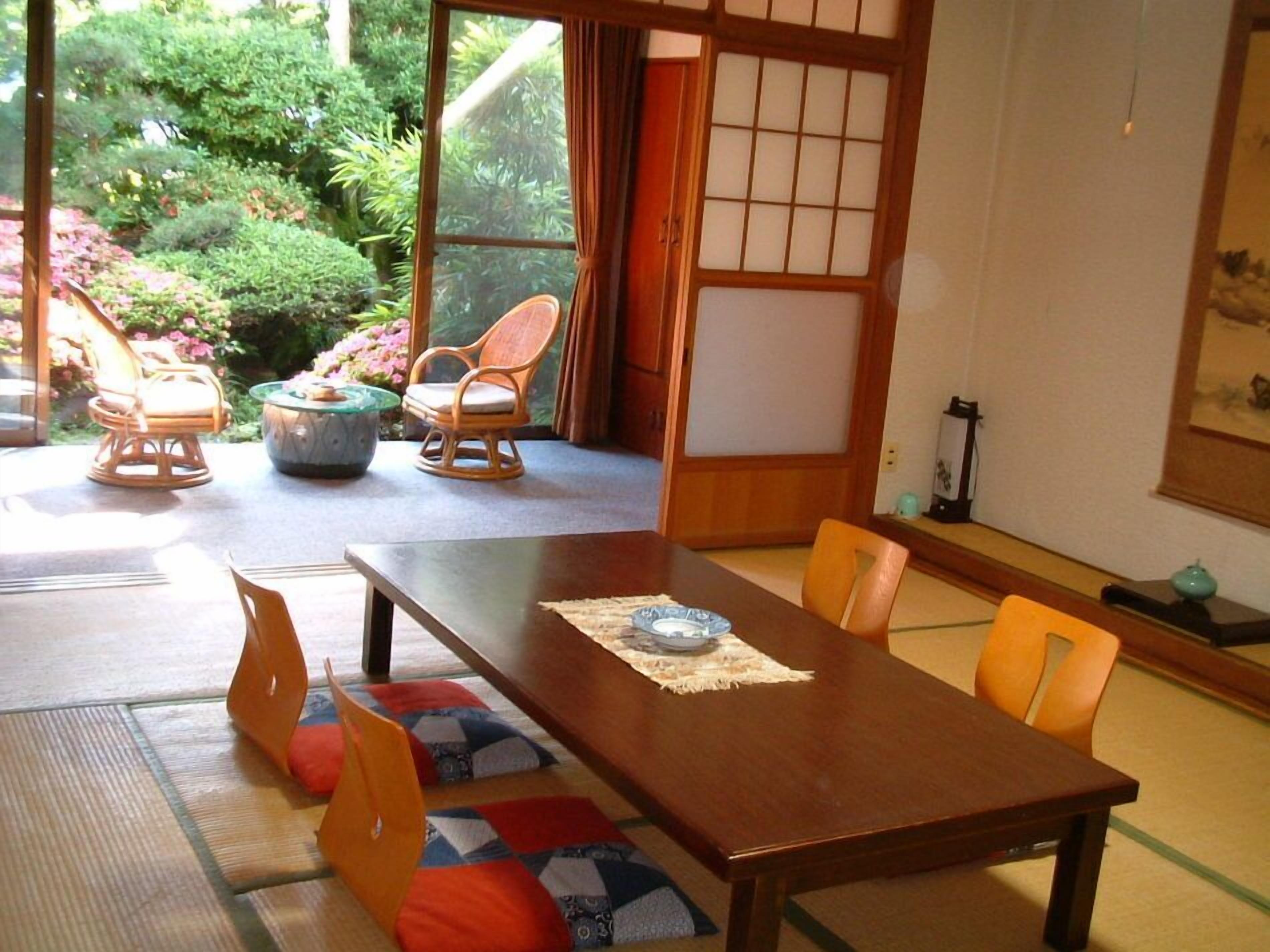 A traditional Japanese-style room with tatami flooring, a low wooden table, and a view of a garden through a sliding door.