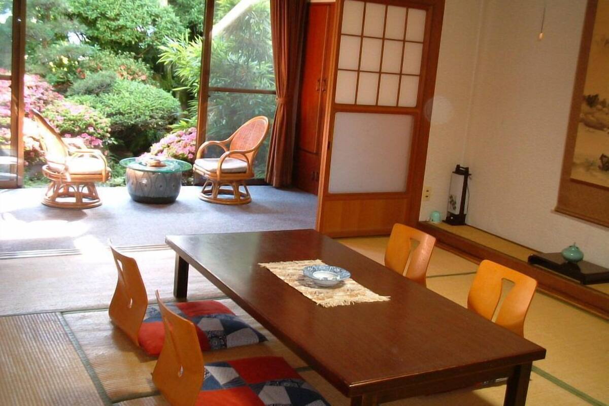 A traditional Japanese-style room with tatami flooring, a low wooden table, and a view of a garden through a sliding door.