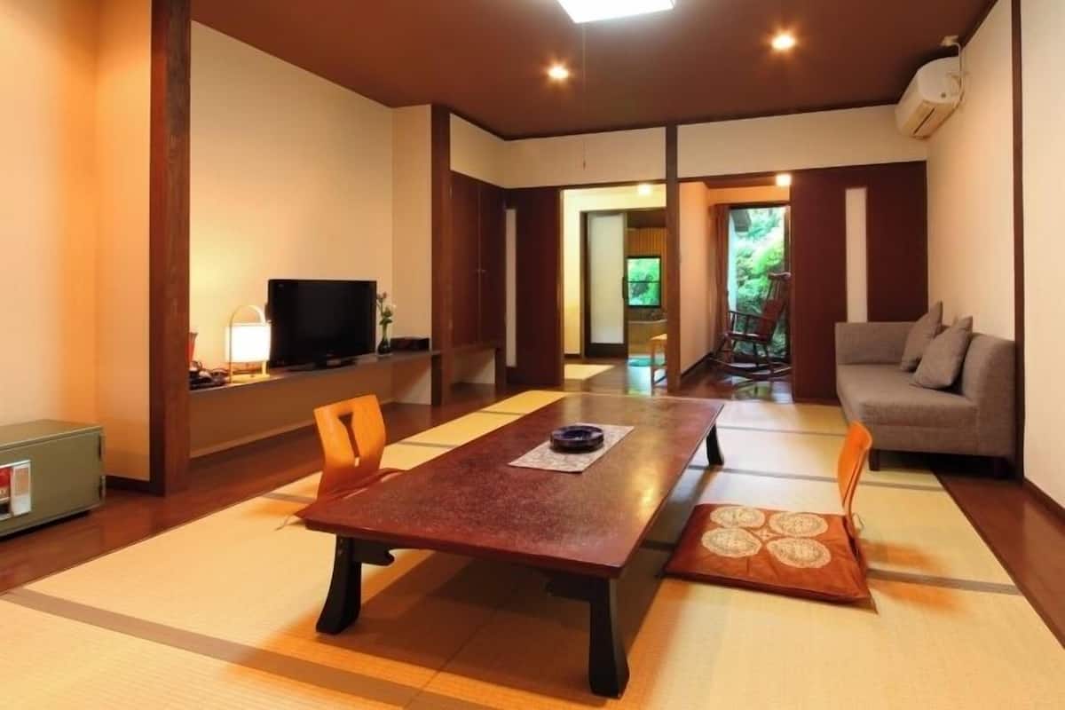 A traditional Japanese-style room with tatami flooring, a low table, a sofa, and a television.