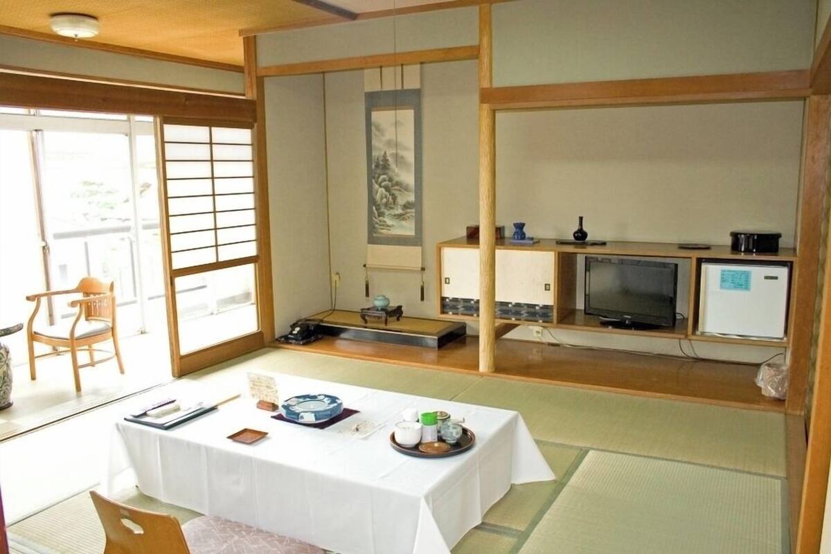 A traditional Japanese room with tatami flooring, a tatami mat table, a television, and a sliding door.