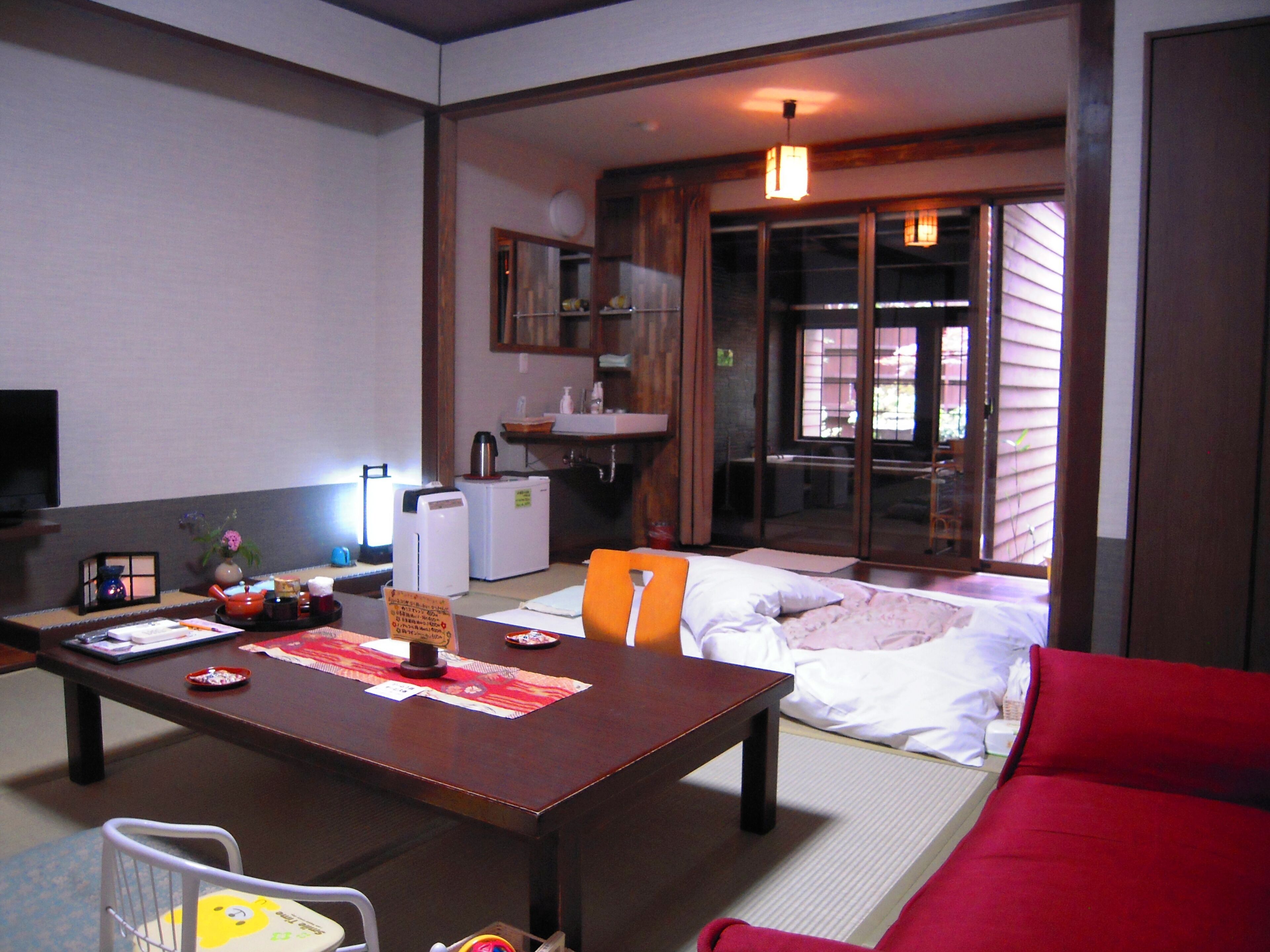 A traditional Japanese-style room with tatami flooring, a low wooden table, a red sofa, and a sliding door leading to a balcony.