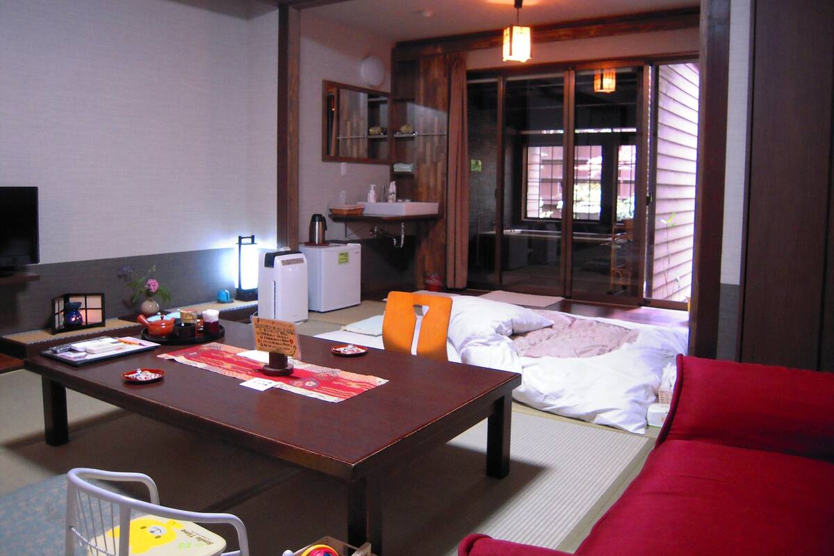 A traditional Japanese-style room with tatami flooring, a low wooden table, a red sofa, and a sliding door leading to a balcony.