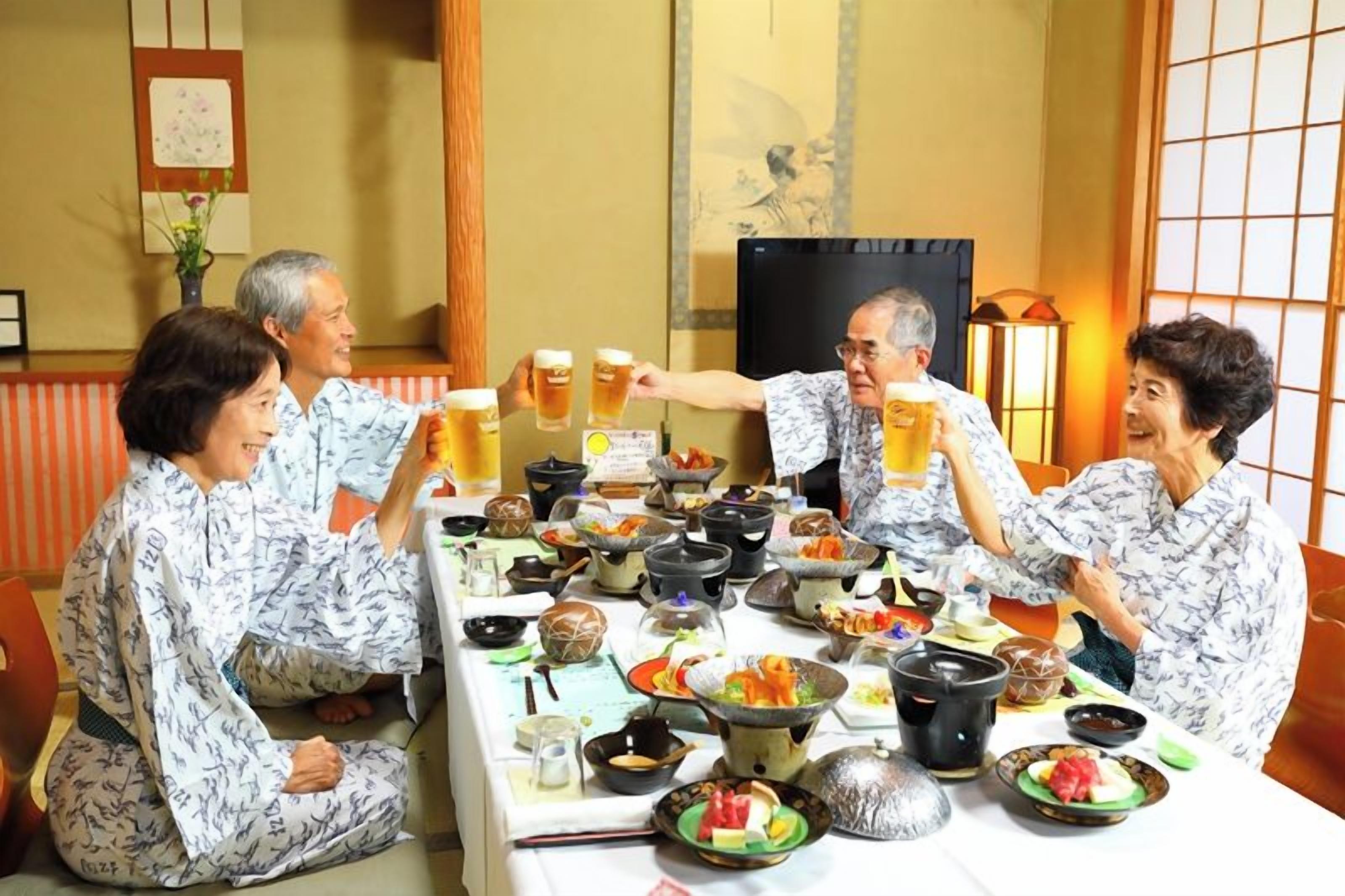 Un grupo de personas sentadas alrededor de una mesa con diversos platos y bebidas, en una habitación con decoración tradicional.