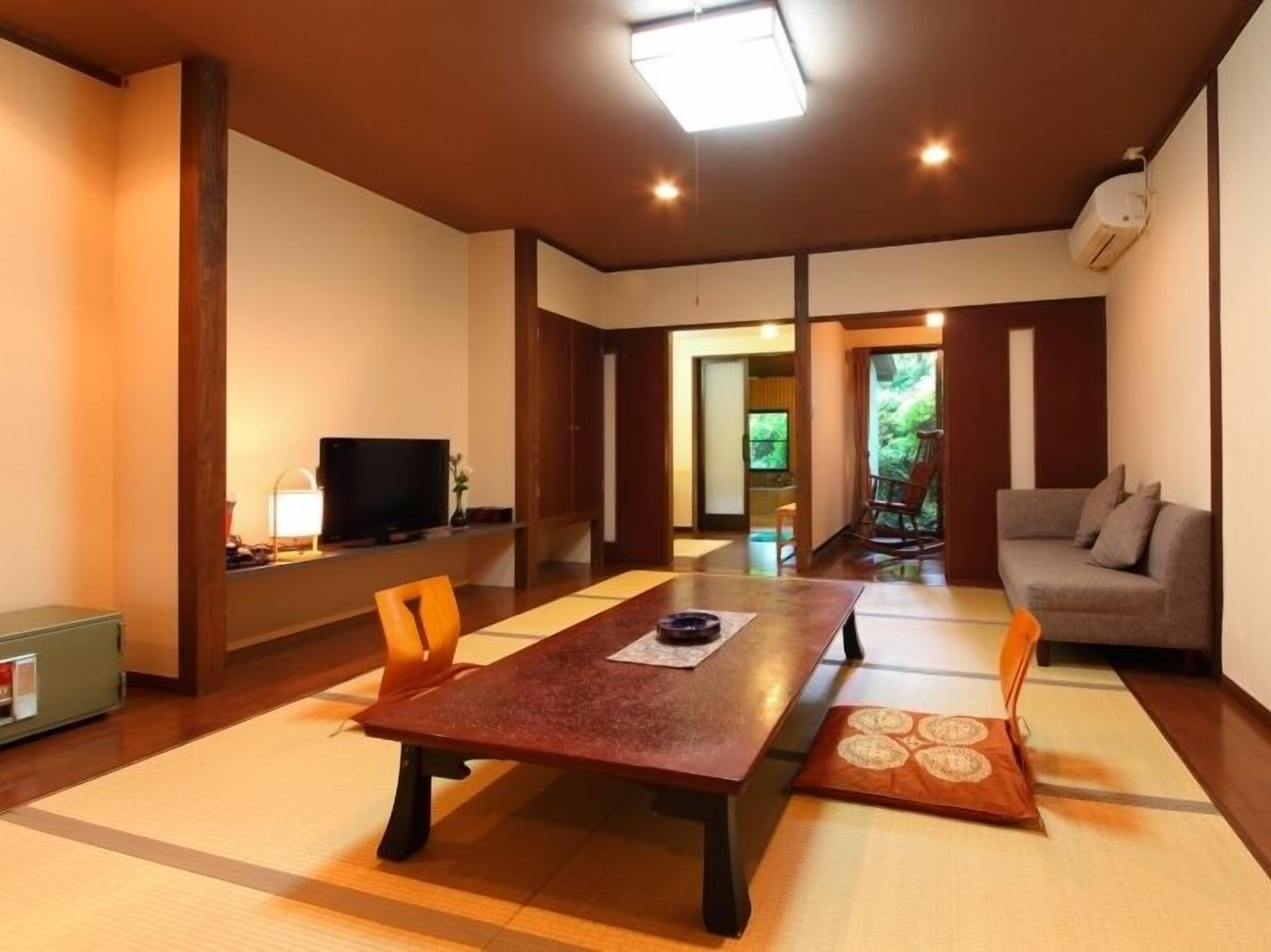 A traditional Japanese-style room with tatami flooring, a low table, a sofa, and a television.