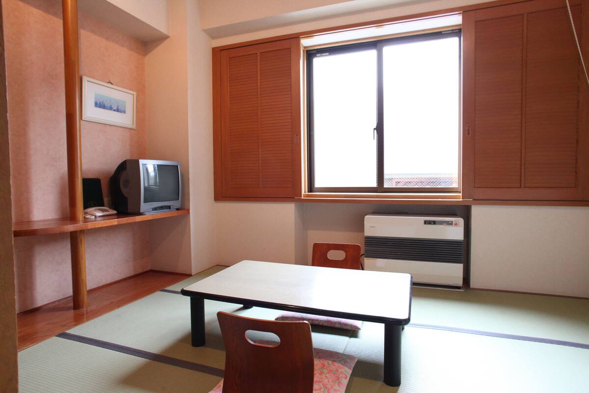 Quarto com piso de tatame, uma mesa baixa, televisão e porta deslizante.