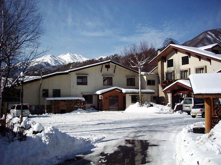 Edificio de dos pisos con tejado cubierto de nieve y un camino de acceso a un estacionamiento.