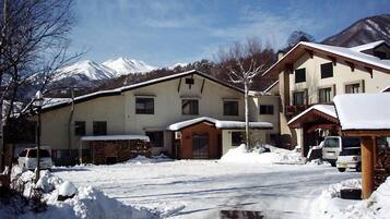 Edificio de dos pisos con tejado cubierto de nieve y un camino de acceso a un estacionamiento.