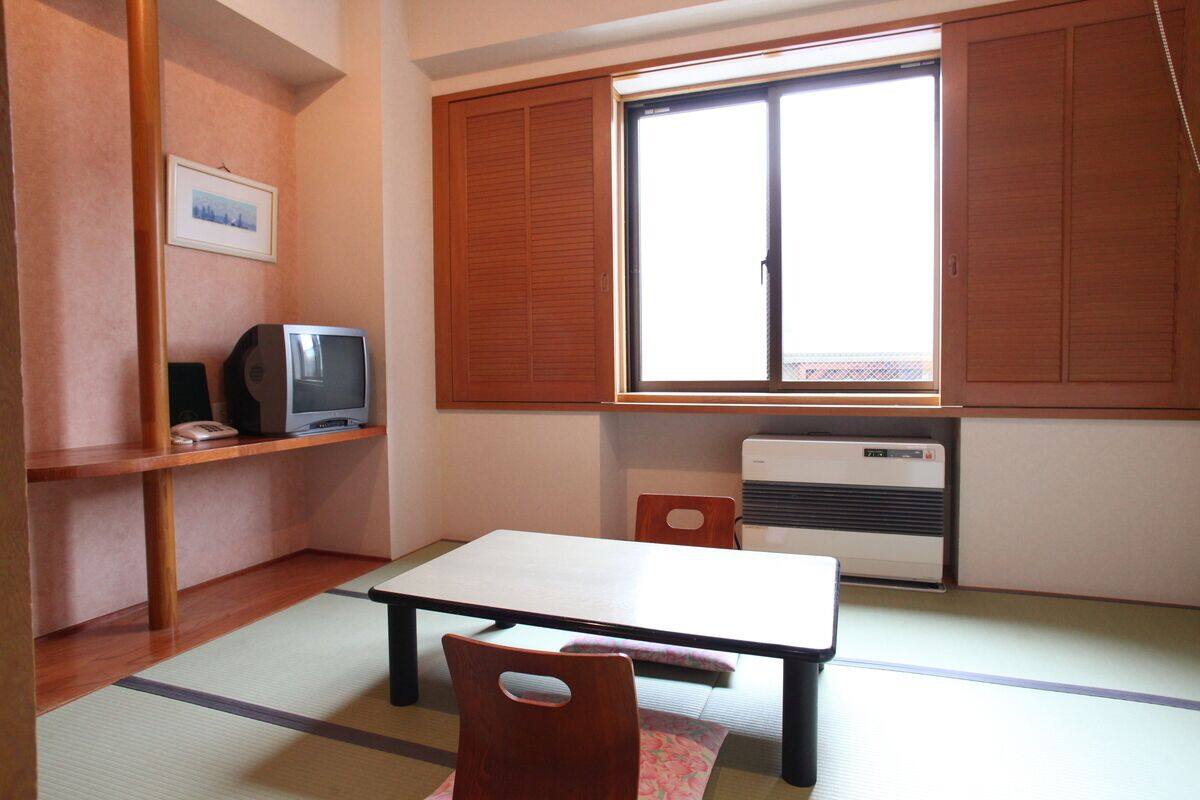 Quarto com piso de tatame, uma mesa baixa, televisão e porta deslizante.
