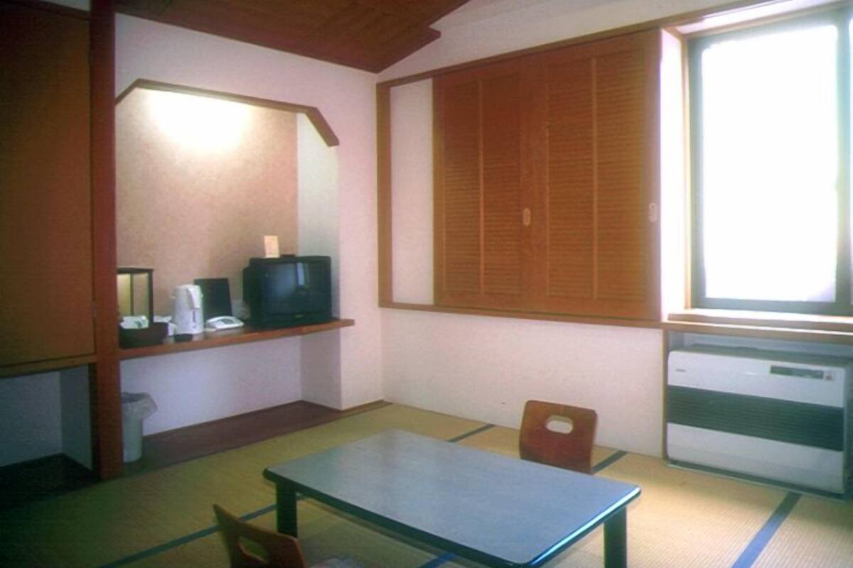 Um quarto pequeno com uma mesa, uma cadeira, uma televisão e uma janela.
