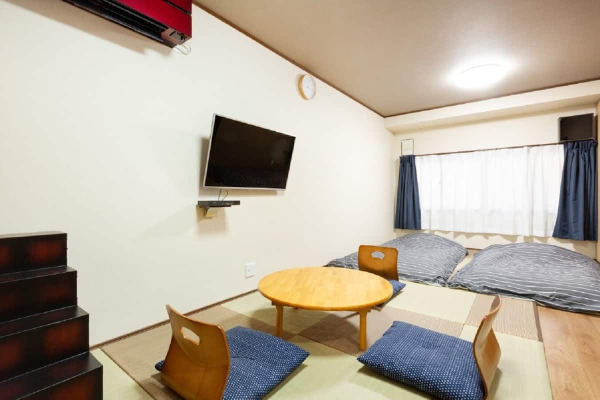 Ein Zimmer mit Fernseher, einem runden Tisch, einer Couch und einer Treppe.