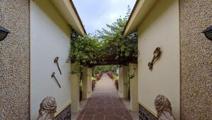 A corridor with a tiled floor, a pergola with climbing plants, and statues on either side. - Amã£ Stays & Trails Nine Palms, Alibag (Alibag)