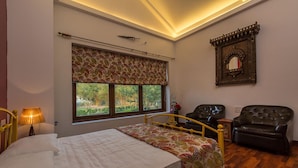 A bedroom with a bed, two chairs, a window with a patterned valance, and a decorative mirror. - Amã£ Stays & Trails Nine Palms, Alibag (Alibag)