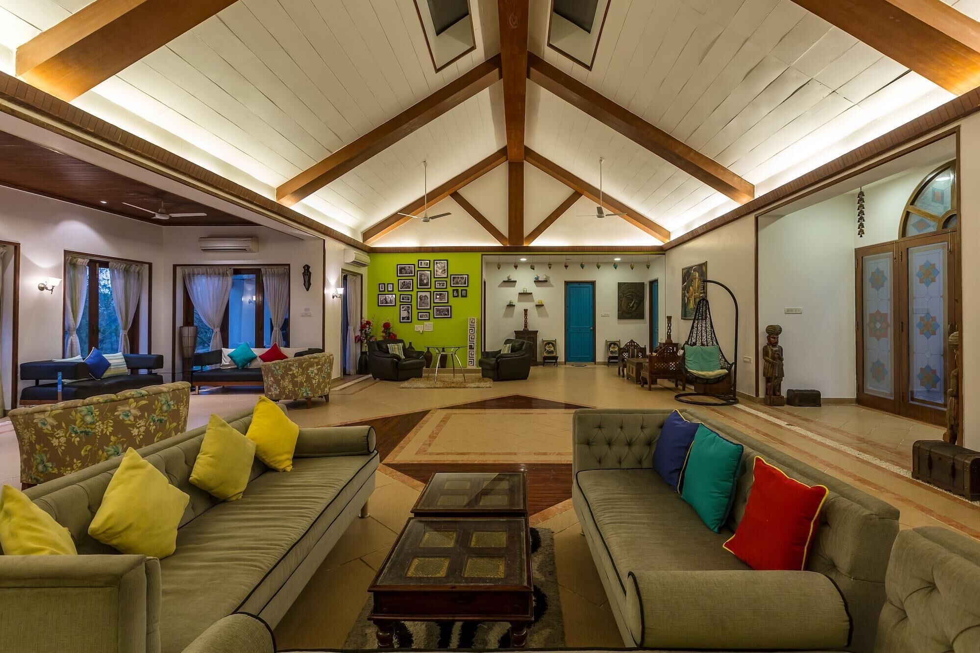A spacious living room with high ceilings, multiple seating areas, and a green accent wall with framed pictures.