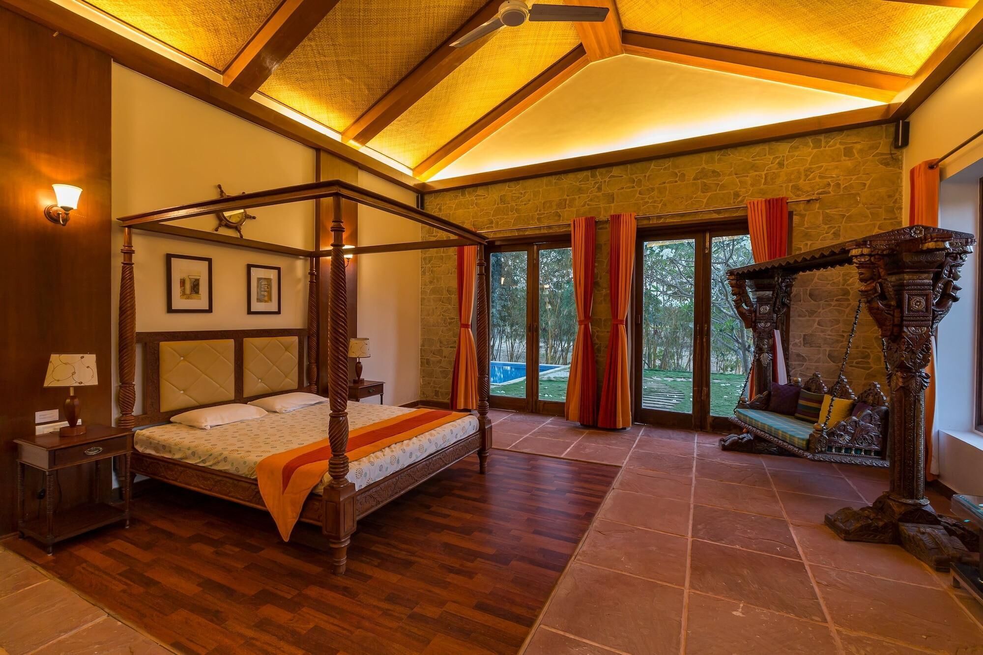 A four-poster bed with a wooden frame and a canopy, a stone wall, and a view of the outdoors through large sliding doors.