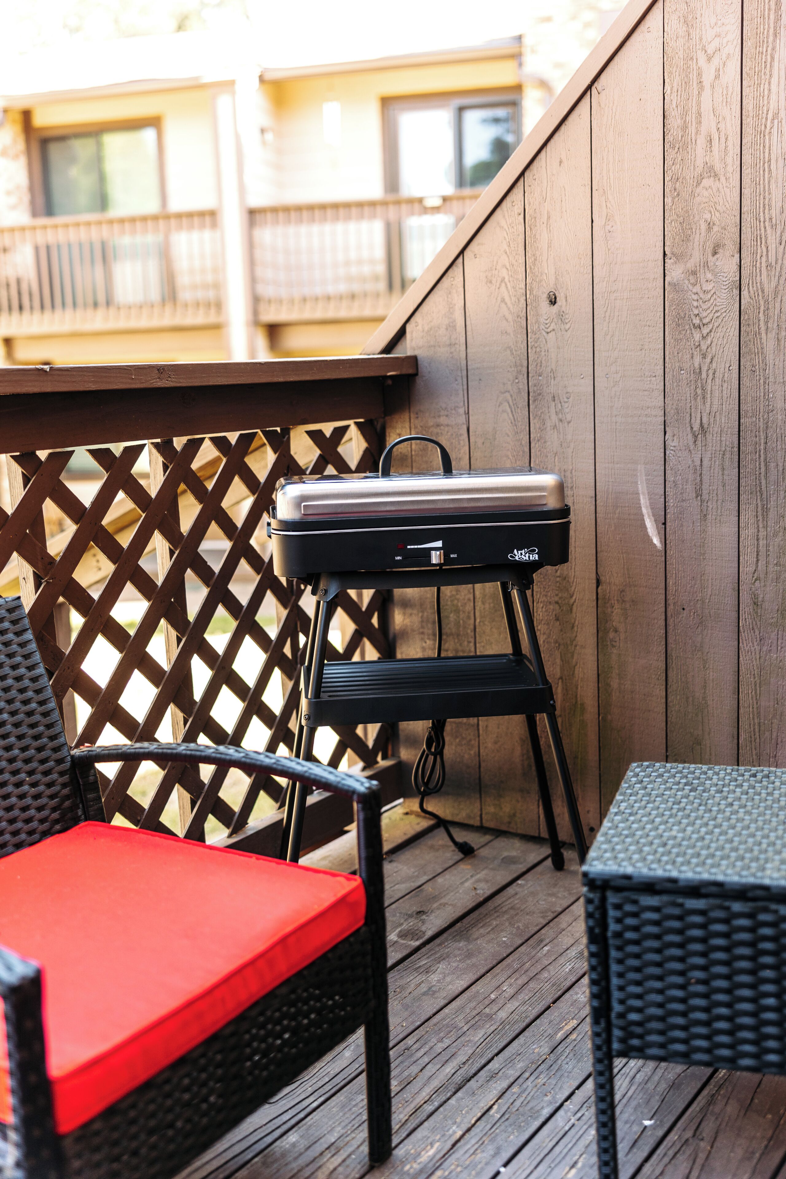 Une terrasse en bois avec un barbecue, des chaises en osier et une petite table.