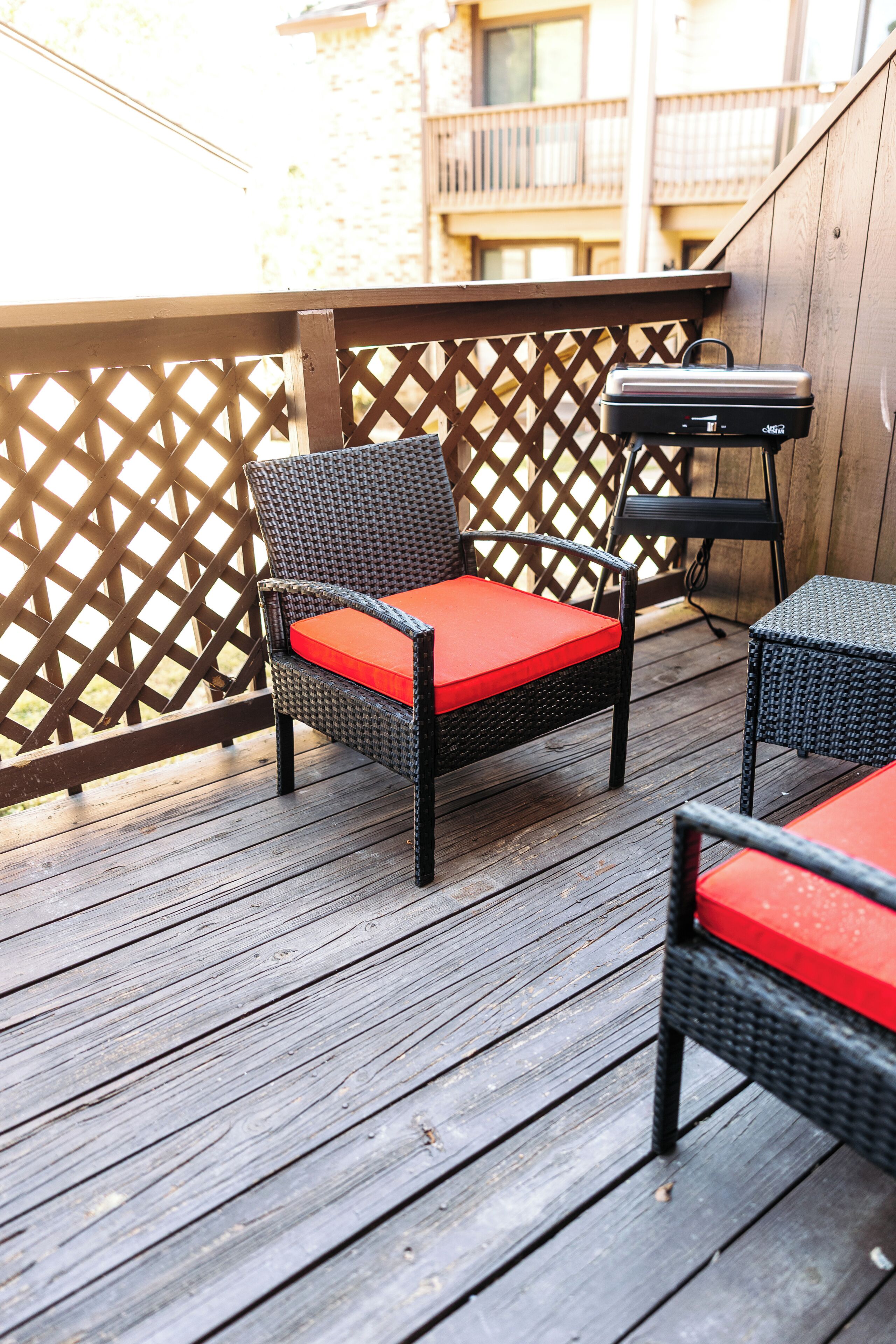 Een houten terras met rieten stoelen en een barbecue.