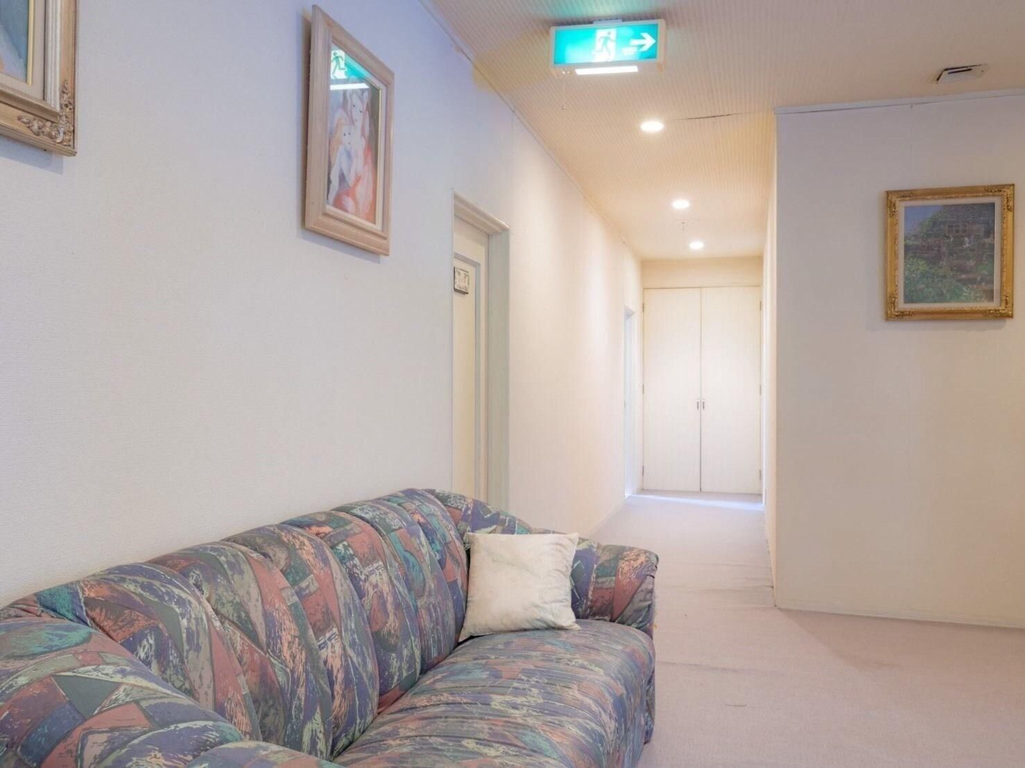 A hallway with a sofa, framed pictures, and a door leading to another room.