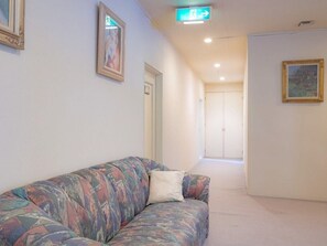 A hallway with a sofa, framed pictures, and a door leading to another room. - Guesthouse Curry Village (Kiryu)