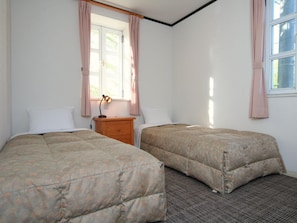 Une chambre avec deux lits, une table de chevet, une lampe et une fenêtre avec des rideaux.