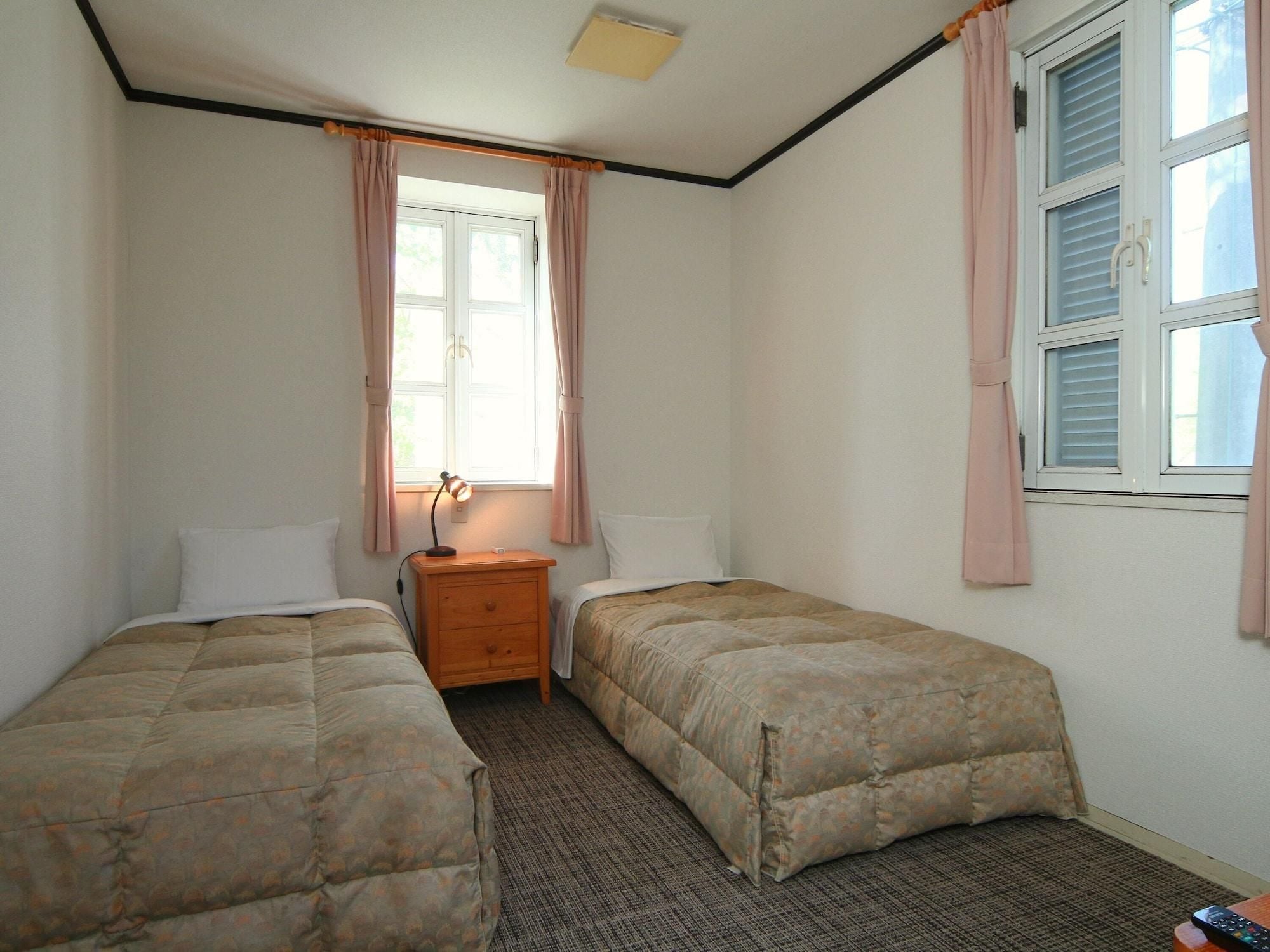 A bedroom with two single beds, a nightstand with a lamp, a window with curtains, and a carpeted floor.