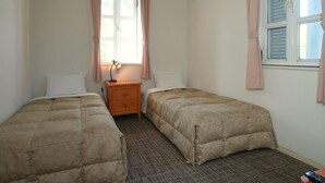 Une chambre avec deux lits simples, une table de chevet avec une lampe, une fenêtre avec des rideaux et un sol recouvert d’une moquette.