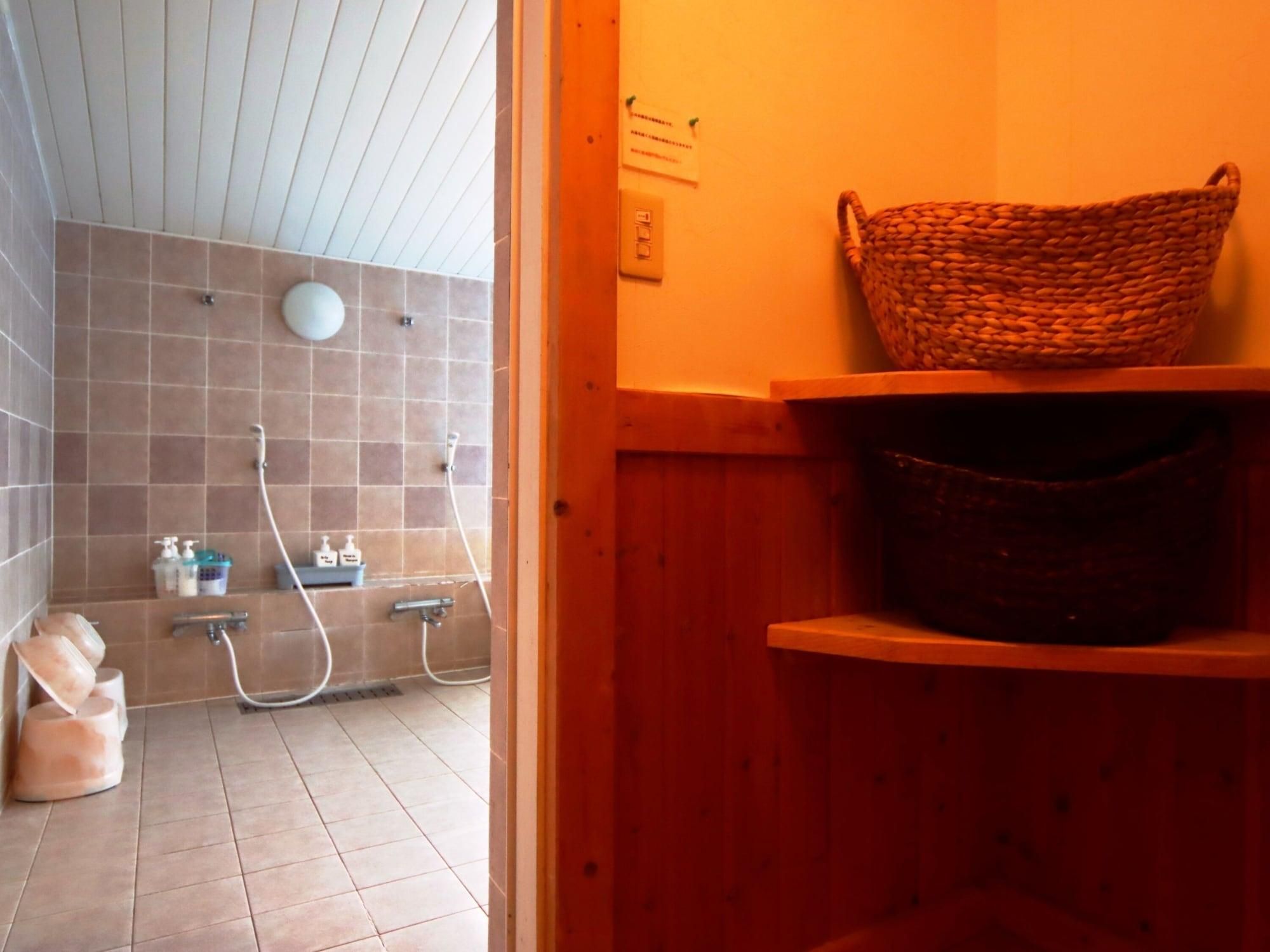 Un baño con ducha, un estante de madera con cestas y piso de azulejos.