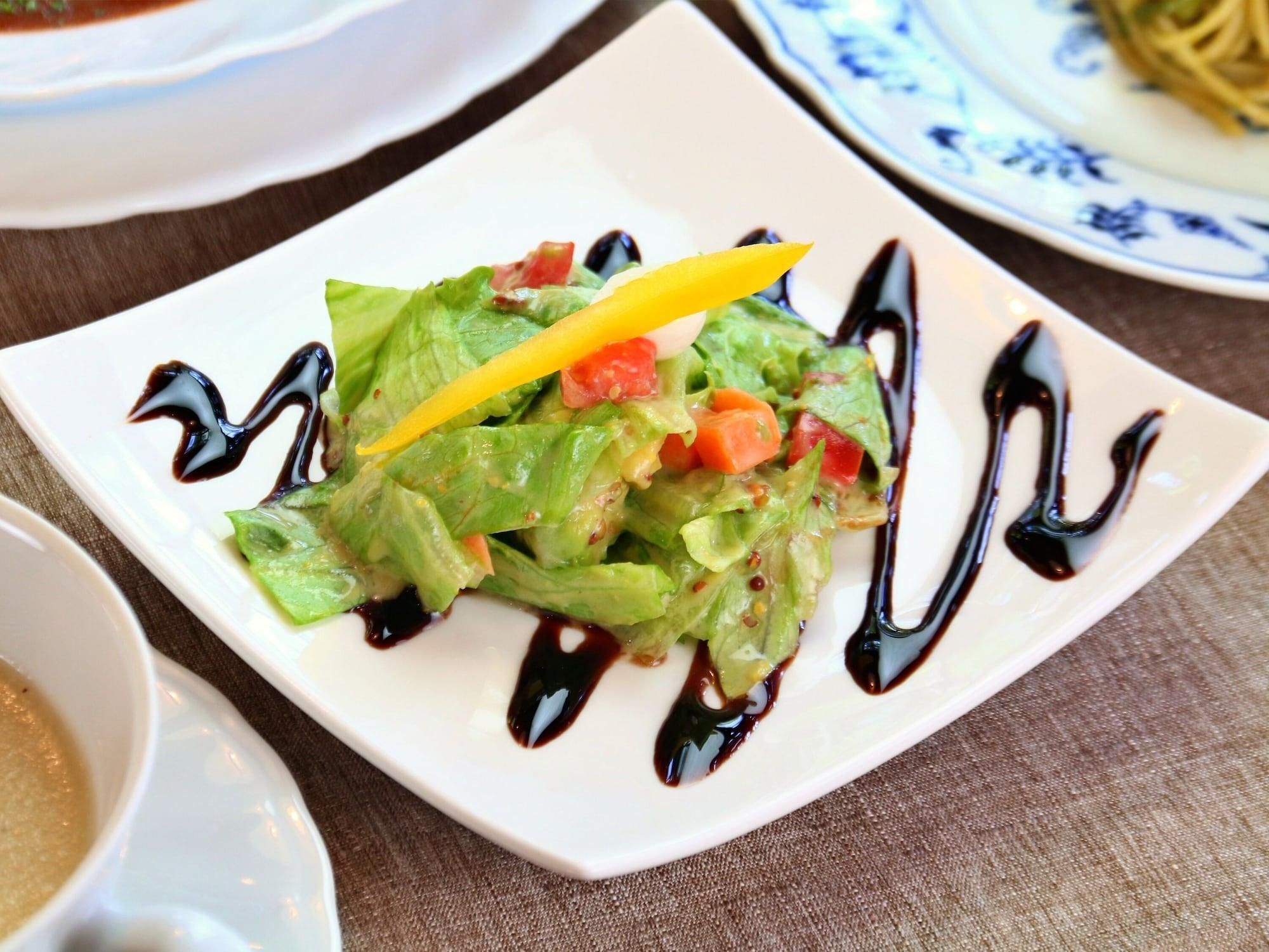 A square white plate with a salad, a yellow pepper, and dark sauce.
