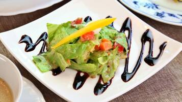 A square white plate with a salad, a yellow pepper, and dark sauce.