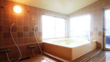 A bathroom with a large bathtub, two showerheads, and a window providing natural light.