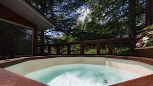 A hot tub surrounded by a wooden deck with a glass enclosure, set against a backdrop of tall trees. - Guesthouse Curry Village (Kiryu)