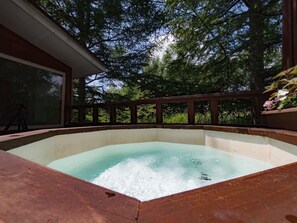A hot tub surrounded by a wooden deck with a glass enclosure, set against a backdrop of tall trees. - Guesthouse Curry Village (Kiryu)