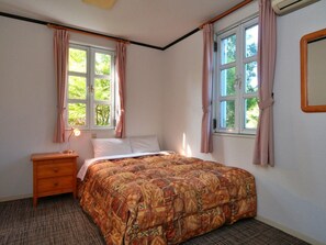 Une chambre à coucher comprenant un lit, une table de chevet, deux fenêtres avec des rideaux et un miroir fixé au mur.